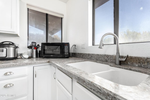 kitchen featuring light stone countertops, sink, and white cabinets