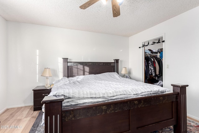 bedroom featuring ceiling fan, a textured ceiling, a walk in closet, a closet, and light wood-type flooring