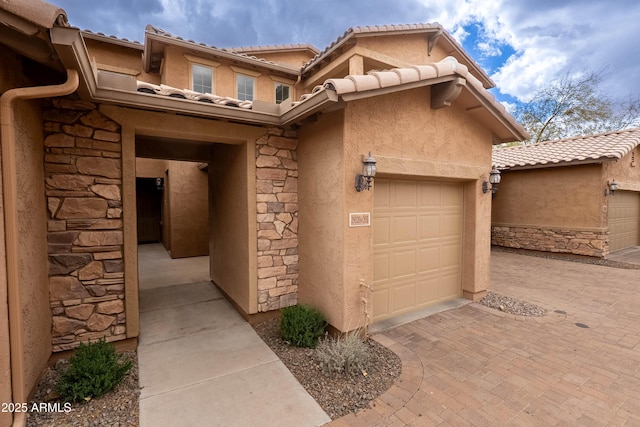 view of exterior entry with a tile roof, stucco siding, decorative driveway, a garage, and stone siding