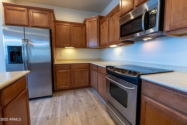 kitchen with light wood-style flooring, brown cabinets, stainless steel appliances, and light countertops