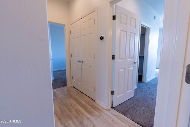 hall featuring baseboards, light colored carpet, and light wood-style flooring