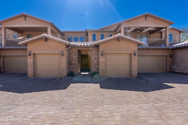 view of property featuring a balcony, decorative driveway, an attached garage, and stucco siding