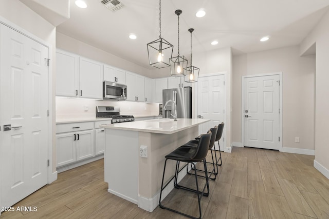 kitchen featuring stainless steel appliances, a sink, light countertops, white cabinetry, and light wood finished floors