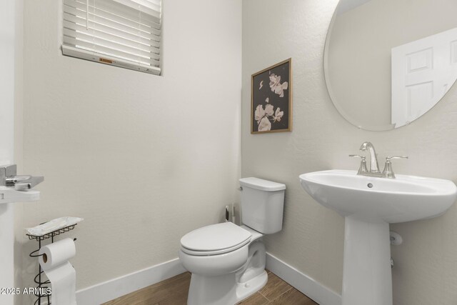 half bath featuring wood finished floors, toilet, baseboards, and a sink