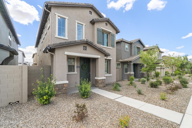 view of front facade featuring fence, stucco siding, and stone siding