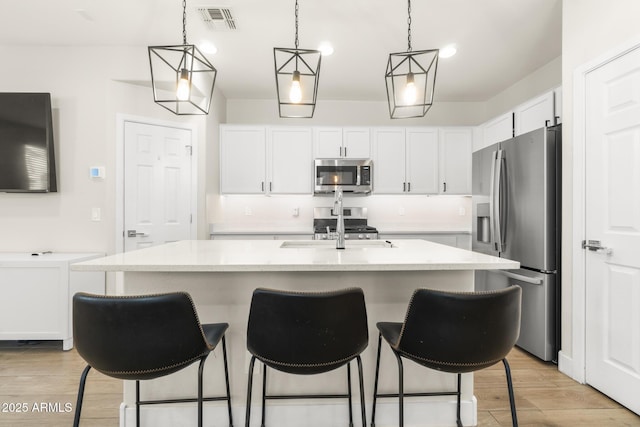 kitchen with appliances with stainless steel finishes, white cabinets, a kitchen bar, light wood finished floors, and pendant lighting