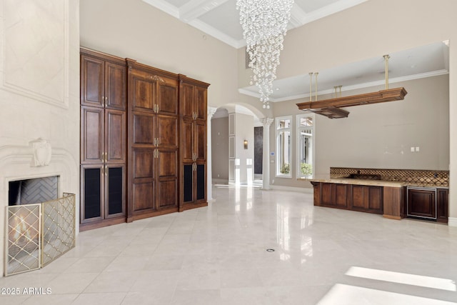 kitchen featuring crown molding, dark brown cabinets, a towering ceiling, and a notable chandelier