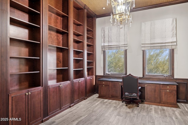 unfurnished office featuring ornamental molding, built in desk, a notable chandelier, and light hardwood / wood-style floors