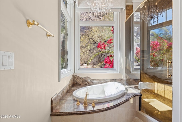 bathroom with tiled tub and a notable chandelier