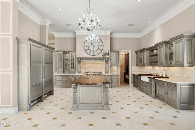 kitchen with crown molding, gray cabinets, a notable chandelier, a towering ceiling, and a large island