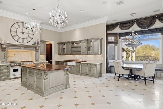 kitchen with an island with sink, butcher block counters, sink, double oven range, and an inviting chandelier