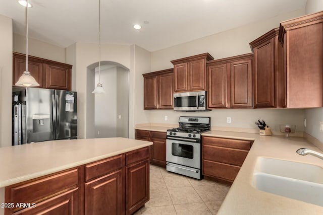 kitchen with appliances with stainless steel finishes, light countertops, a sink, and decorative light fixtures