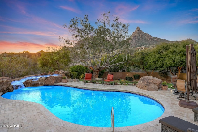 pool at dusk featuring a patio area, pool water feature, and a mountain view