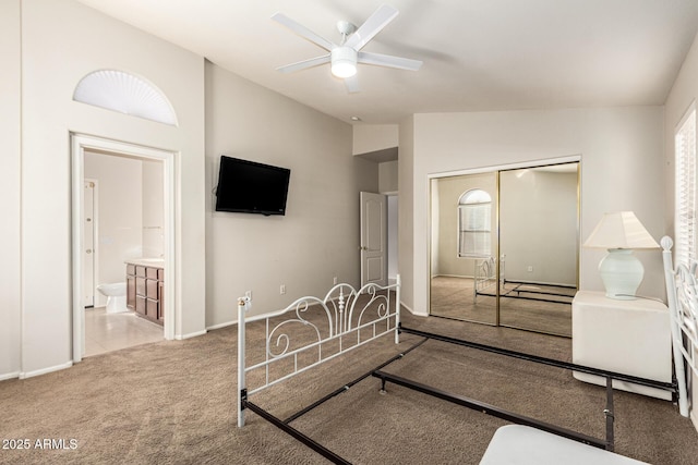 carpeted bedroom with a closet, a ceiling fan, vaulted ceiling, ensuite bath, and baseboards