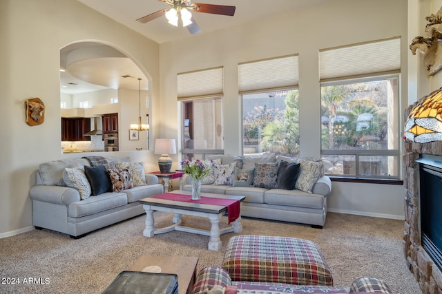 carpeted living room with ceiling fan with notable chandelier and a fireplace