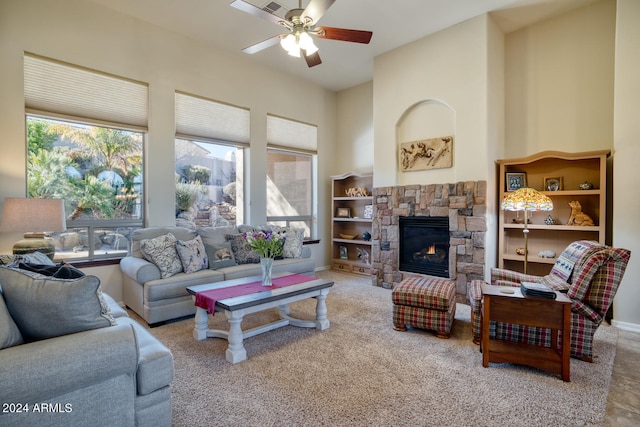 carpeted living room with ceiling fan and a stone fireplace