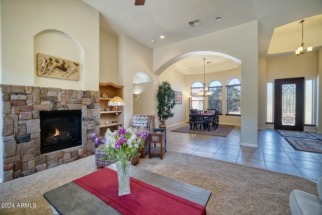 living room with ornamental molding, tile patterned floors, a stone fireplace, and an inviting chandelier