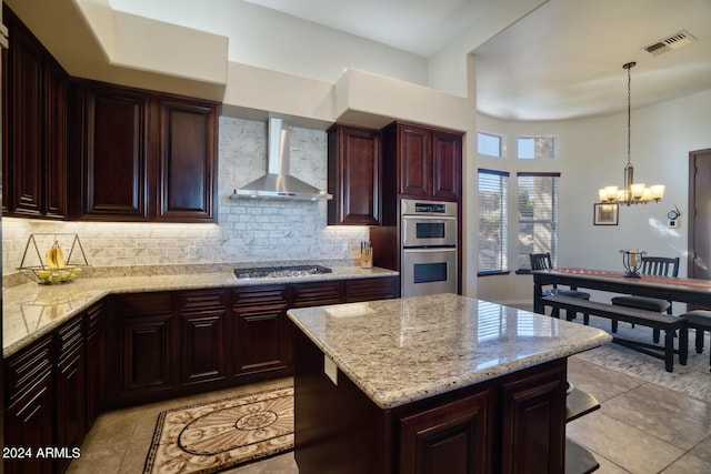 kitchen featuring wall chimney exhaust hood, decorative light fixtures, decorative backsplash, light stone countertops, and appliances with stainless steel finishes