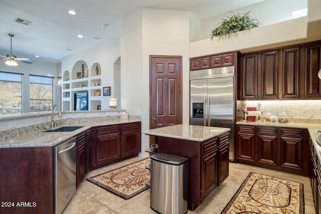 kitchen featuring a center island, sink, light stone counters, appliances with stainless steel finishes, and light tile patterned floors