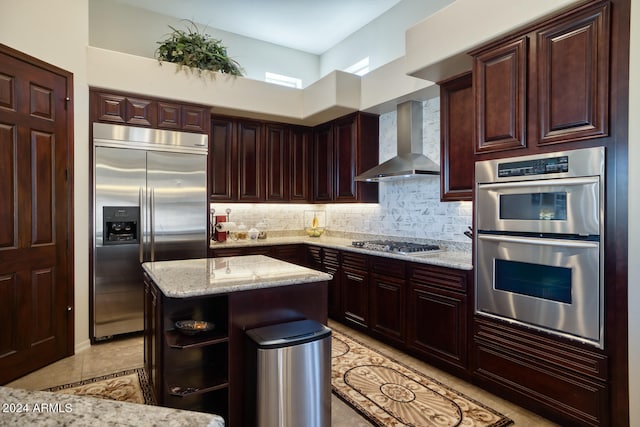 kitchen featuring wall chimney exhaust hood, tasteful backsplash, a kitchen island, light stone counters, and stainless steel appliances