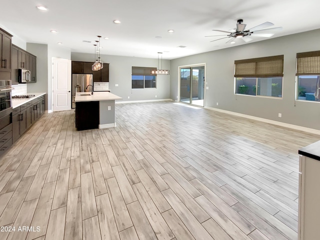 kitchen with appliances with stainless steel finishes, dark brown cabinetry, light hardwood / wood-style floors, and a kitchen island with sink