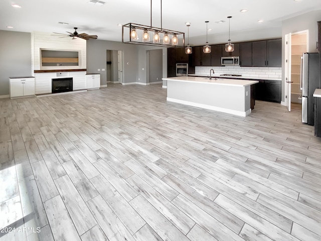 kitchen with ceiling fan, pendant lighting, light hardwood / wood-style floors, a kitchen island with sink, and appliances with stainless steel finishes