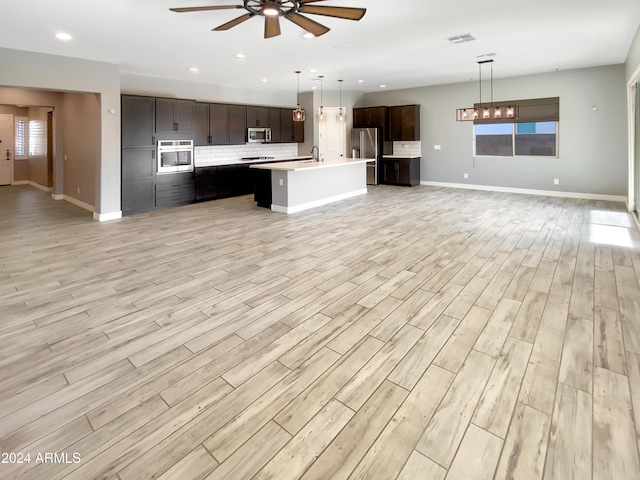 kitchen featuring a kitchen island with sink, light hardwood / wood-style floors, decorative light fixtures, and appliances with stainless steel finishes