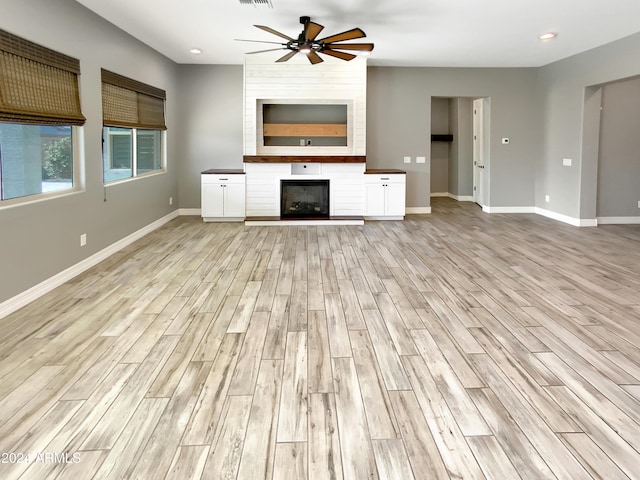 unfurnished living room with ceiling fan, a fireplace, and light wood-type flooring