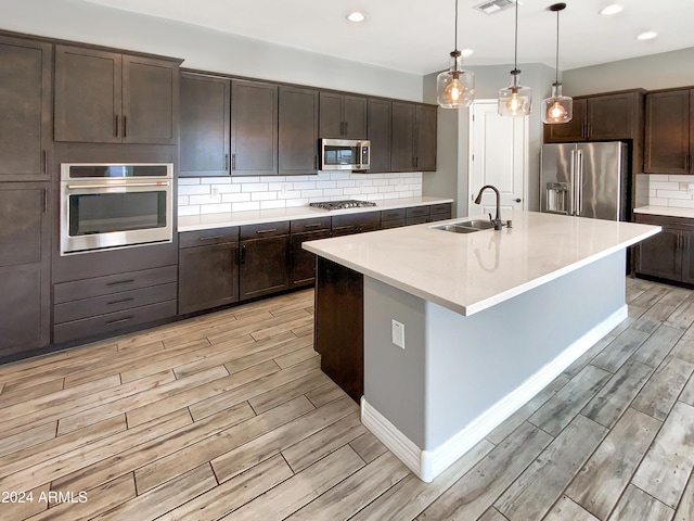 kitchen featuring light hardwood / wood-style floors, sink, appliances with stainless steel finishes, and an island with sink