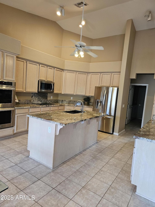 kitchen featuring stainless steel appliances, sink, a kitchen island with sink, light stone counters, and light tile patterned floors