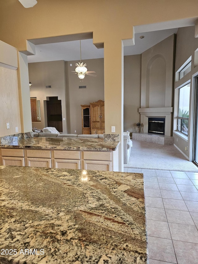 kitchen featuring ceiling fan, a large fireplace, a high ceiling, hanging light fixtures, and light tile patterned floors