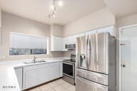 kitchen featuring sink, light tile patterned floors, stainless steel fridge with ice dispenser, white cabinets, and range