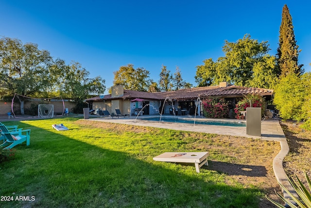 rear view of property with a tile roof, a patio area, an outdoor pool, and a chimney