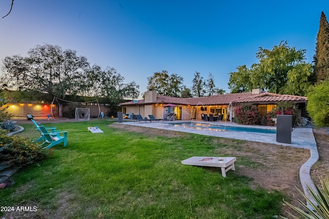 rear view of house featuring a patio, an outdoor pool, a chimney, a tile roof, and a lawn