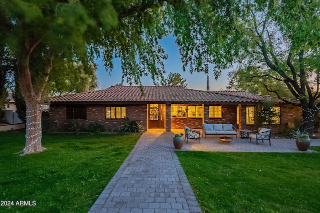 view of front of property with a lawn, an outdoor living space, a patio, brick siding, and a tiled roof