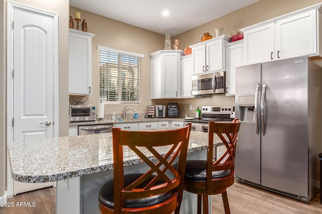 kitchen featuring white cabinetry, stainless steel appliances, a kitchen bar, a kitchen island, and light wood-type flooring