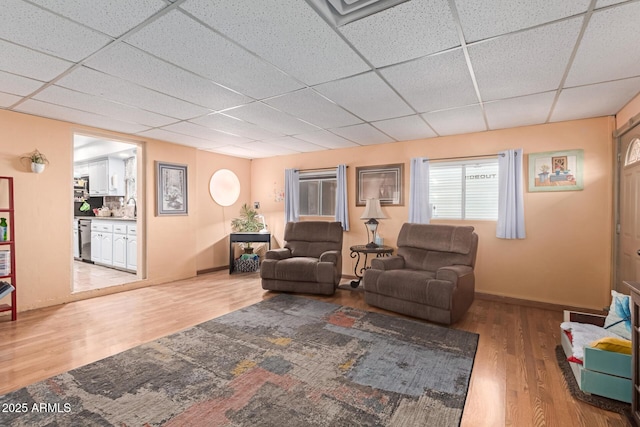 living area featuring baseboards, a paneled ceiling, and wood finished floors