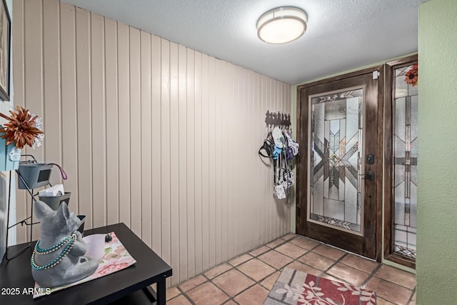 foyer entrance featuring light tile patterned floors, a textured wall, wood walls, and a textured ceiling