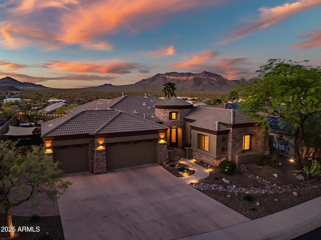 prairie-style house featuring a tile roof, stone siding, a garage, a mountain view, and driveway