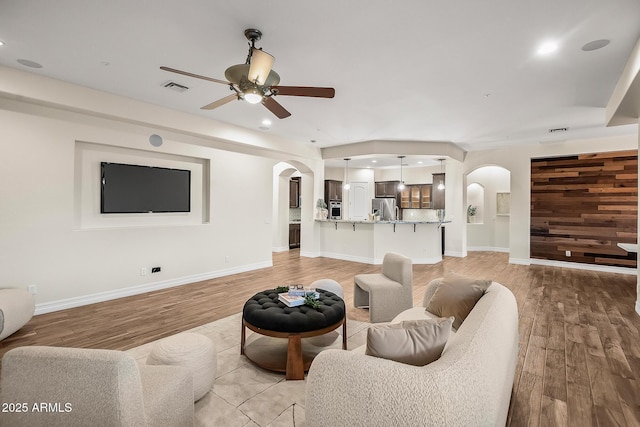 living area with light wood-style floors, arched walkways, ceiling fan, and visible vents