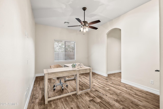 office space with arched walkways, baseboards, a ceiling fan, and wood finished floors