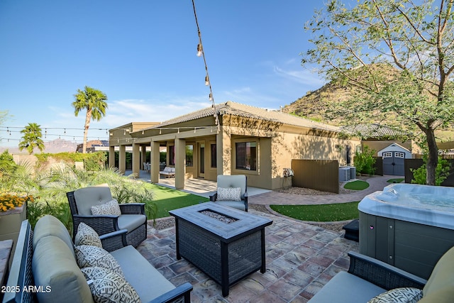 view of patio featuring a storage shed, an outbuilding, central AC unit, a hot tub, and an outdoor living space with a fire pit
