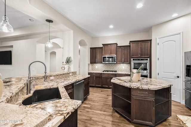 kitchen with backsplash, appliances with stainless steel finishes, arched walkways, dark brown cabinets, and a sink
