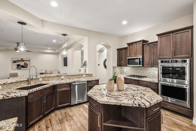 kitchen with light stone counters, a sink, light wood-style floors, stainless steel appliances, and decorative backsplash