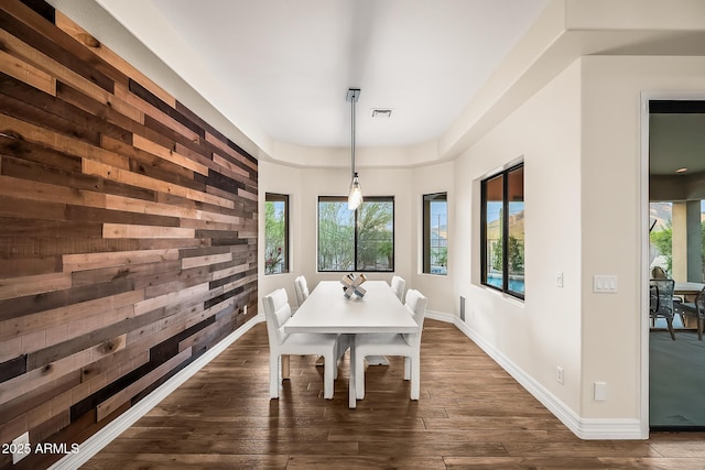 dining room featuring visible vents, dark wood finished floors, a raised ceiling, baseboards, and wooden walls