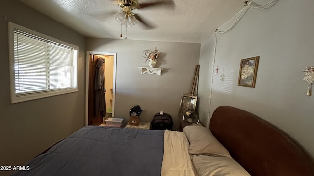 bedroom with a textured ceiling, a walk in closet, and ceiling fan