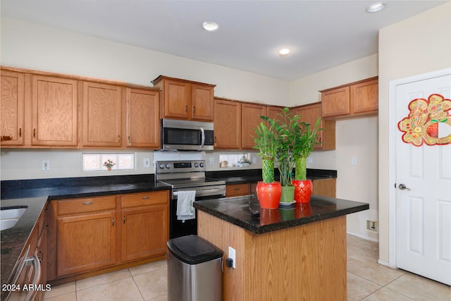 kitchen with appliances with stainless steel finishes, dark stone counters, light tile flooring, and a kitchen island