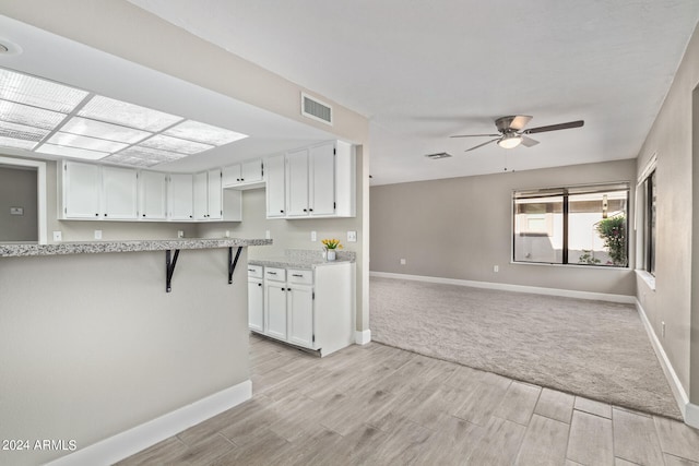 kitchen with light stone counters, ceiling fan, light carpet, white cabinetry, and a kitchen breakfast bar