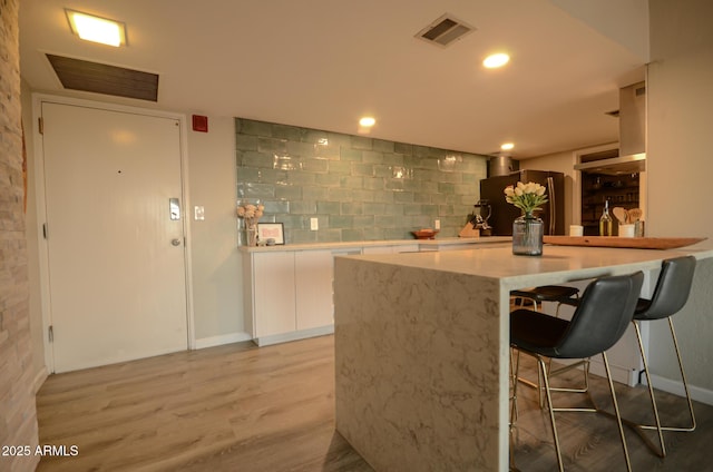 kitchen featuring a breakfast bar area, tasteful backsplash, light wood-type flooring, fridge, and white cabinets