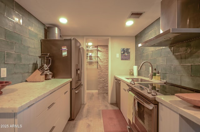 kitchen featuring sink, light wood-type flooring, stainless steel appliances, decorative backsplash, and exhaust hood